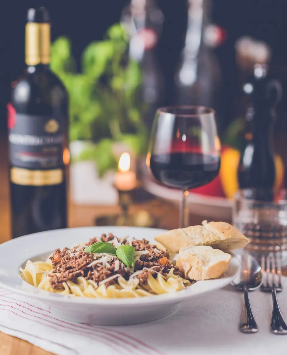 Des pâtes servies à table avec un verre de vin rouge, à la bougie